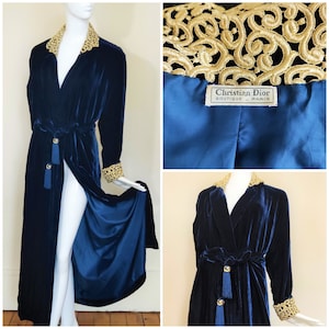 Puede incluir: Una larga bata de terciopelo azul oscuro con ribetes bordados en oro alrededor del cuello y las mangas. La bata tiene un cinturón de lazo y lleva una etiqueta que dice "Christian Dior Boutique - Paris".
