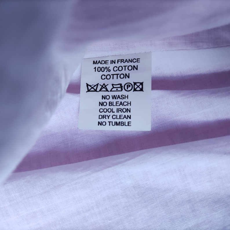 May include: White care label with black text that reads "Made in France 100% Coton Cotton" and a series of symbols indicating that the garment should not be washed, bleached, ironed, or tumbled dried. The label also states that the garment should be dry cleaned.