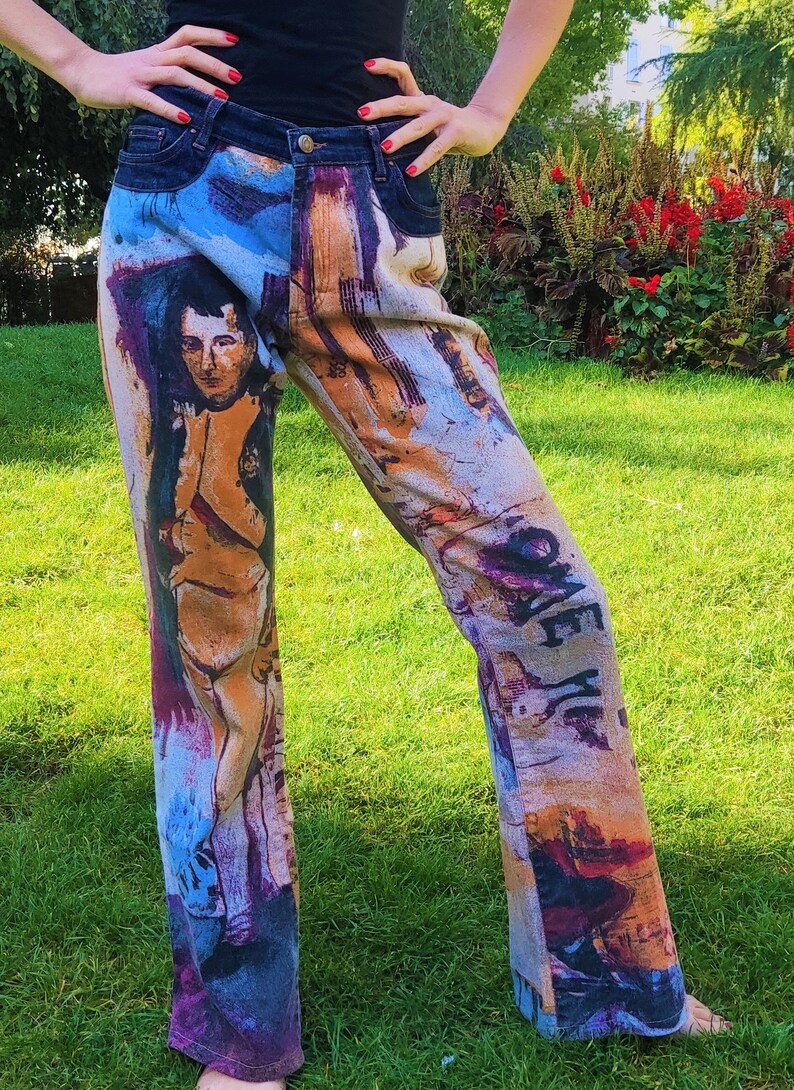 May include: Blue denim jeans with a colorful abstract print featuring a portrait of a person. The print includes a variety of colors, including blue, orange, yellow, and purple.