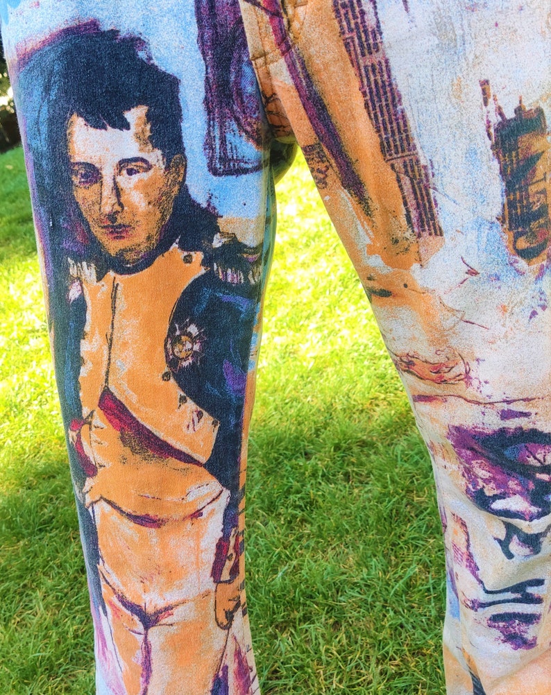 May include: A pair of pants with a colorful, abstract print featuring a portrait of a man in a military uniform. The print includes shades of blue, purple, orange, and white.