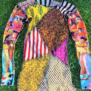 Può includere: Una camicia a maniche lunghe realizzata in tessuto patchwork. La camicia è realizzata con tessuti di diversi colori con vari motivi, tra cui motivi floreali, a righe e geometrici. La camicia ha un collo alto e maniche lunghe.