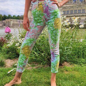 May include: A pair of light blue jeans with a floral print featuring a variety of colors, including pink, yellow, and green. The jeans have a high waist and a skinny fit.