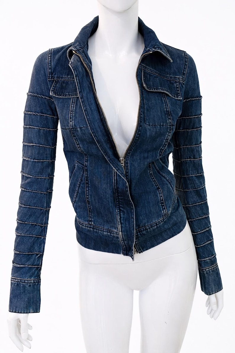 May include: A dark blue denim jacket with a zip-up front, collar, and pockets. The sleeves have a unique design with horizontal stitching. The jacket is displayed on a white mannequin.