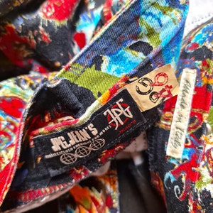 May include: Close-up of a black and red patterned denim jacket with a black label that reads "JPG Jean's" and a white label that reads "Made in Italy".