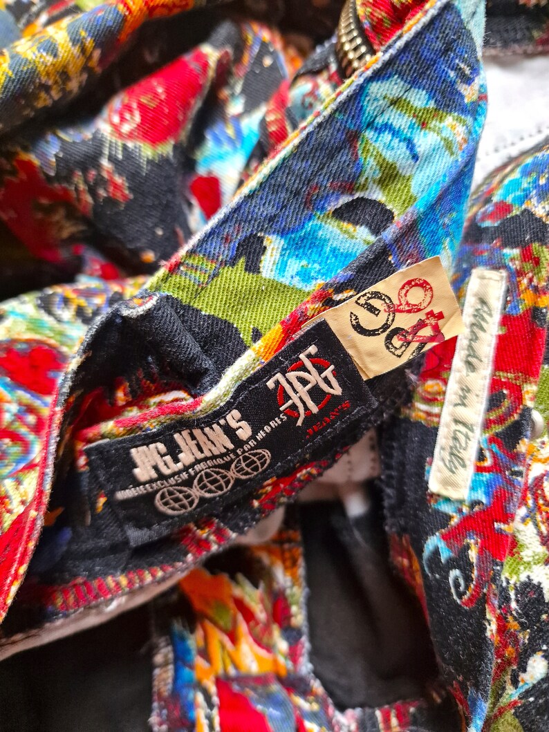 May include: Close-up of a black and red patterned denim jacket with a black label that reads "JPG Jean's" and a white label that reads "Made in Italy".