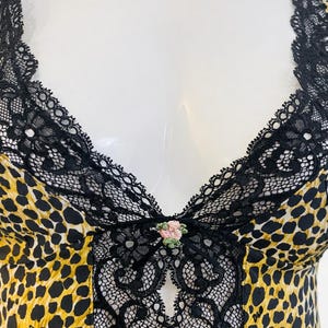 May include: A sleeveless top with a leopard print pattern in yellow and black. The top features black lace trim along the neckline and straps, with a small floral embellishment at the center. The D&G logo is visible.