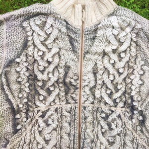 May include: A white knitted sweater with a zipper closure and a cable knit pattern.