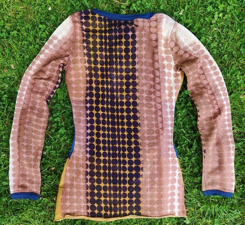 May include: A long-sleeved shirt with a brown and gold polka dot pattern. The shirt has a dark blue neckline and a vertical stripe of dark blue circles down the center.
