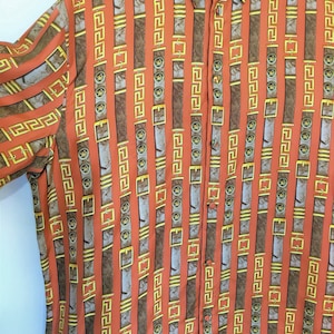 Könnte beinhalten: Ein langärmliges Hemd mit Knöpfen und einem sich wiederholenden Muster aus braunen und goldenen Gürteln mit geometrischem Design. Das Hemd ist leuchtend orange.