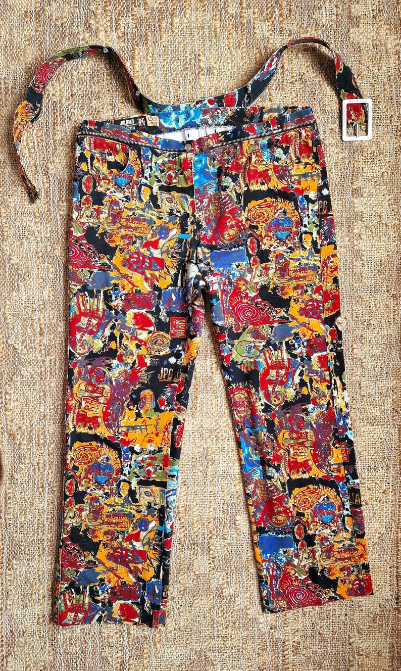 May include: A pair of black pants with a colorful abstract print. The pants have a wide belt with a white buckle.