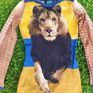 May include: A long-sleeved, brown, yellow, and blue knit sweater with a lion graphic and the text "Jean Paul Gaultier" on the front.