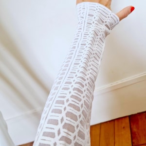 Può includere: Camicia bianca a maniche lunghe con un motivo geometrico. La camicia è realizzata in tessuto trasparente e ha una silhouette aderente.