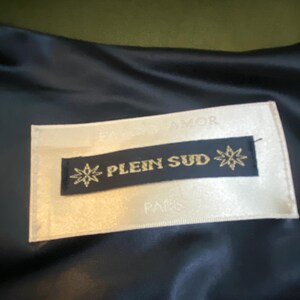 以下が含まれることがあります： 金色の文字で「PLEIN SUD」と書かれたラベルのクローズアップ。黒い背景にスターバーストのデザインがあります。ラベルはクリーム色の背景にあり、下に「PARIS」という文字があります。