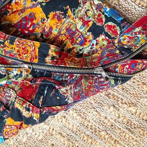 May include: A black fabric bag with a zipper closure. The bag is decorated with a colorful, abstract pattern.