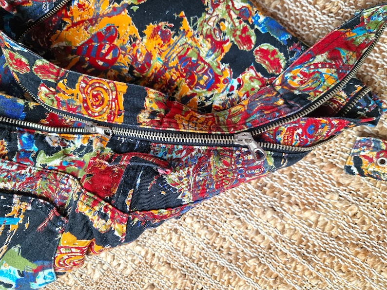 May include: A black fabric bag with a zipper closure. The bag is decorated with a colorful, abstract pattern.