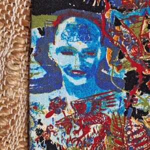 May include: A colorful fabric with a repeating pattern of a blue face with a red and yellow background. The fabric has a textured surface.