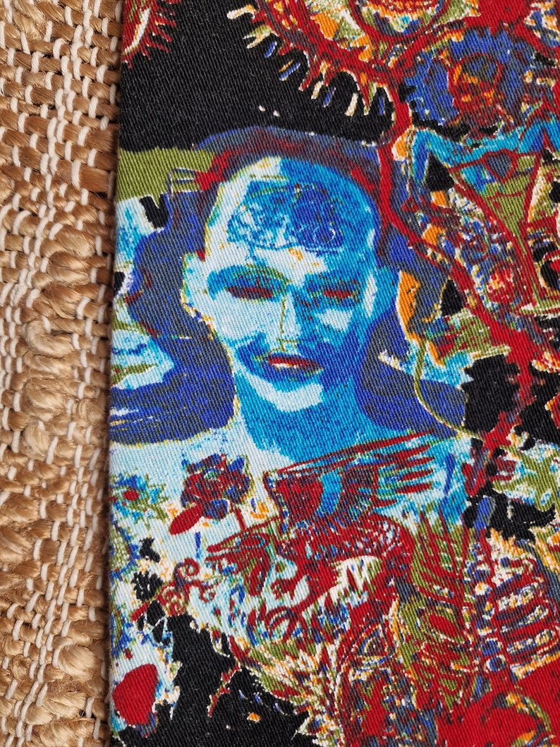 May include: A colorful fabric with a repeating pattern of a blue face with a red and yellow background. The fabric has a textured surface.