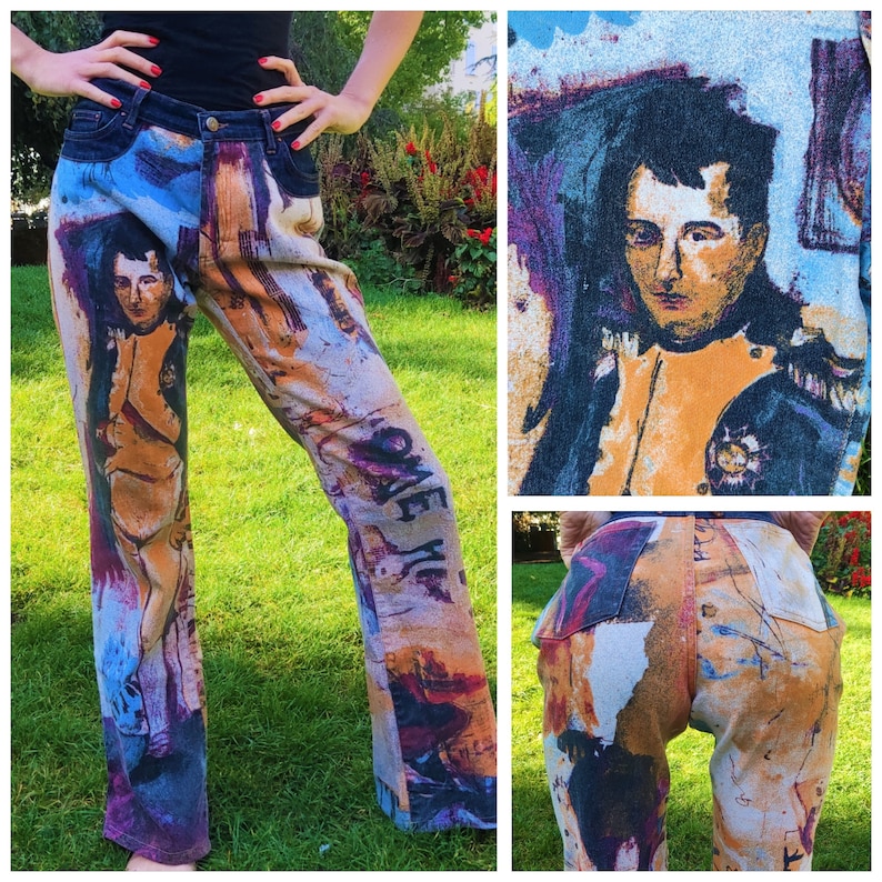 May include: A pair of blue denim jeans with a colorful, abstract print featuring a portrait of a man. The print includes the words "Love Me" on one leg.