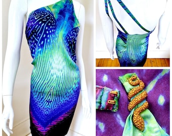May include: A one-shoulder dress with a vibrant blue, green, and purple pattern. The dress is displayed on a mannequin, showcasing its unique design. A gold-colored snake-shaped accessory is also visible.