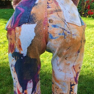 May include: A pair of jeans with a colorful abstract print. The print features a mix of orange, blue, white, and black colors. The jeans have a relaxed fit and a straight leg.