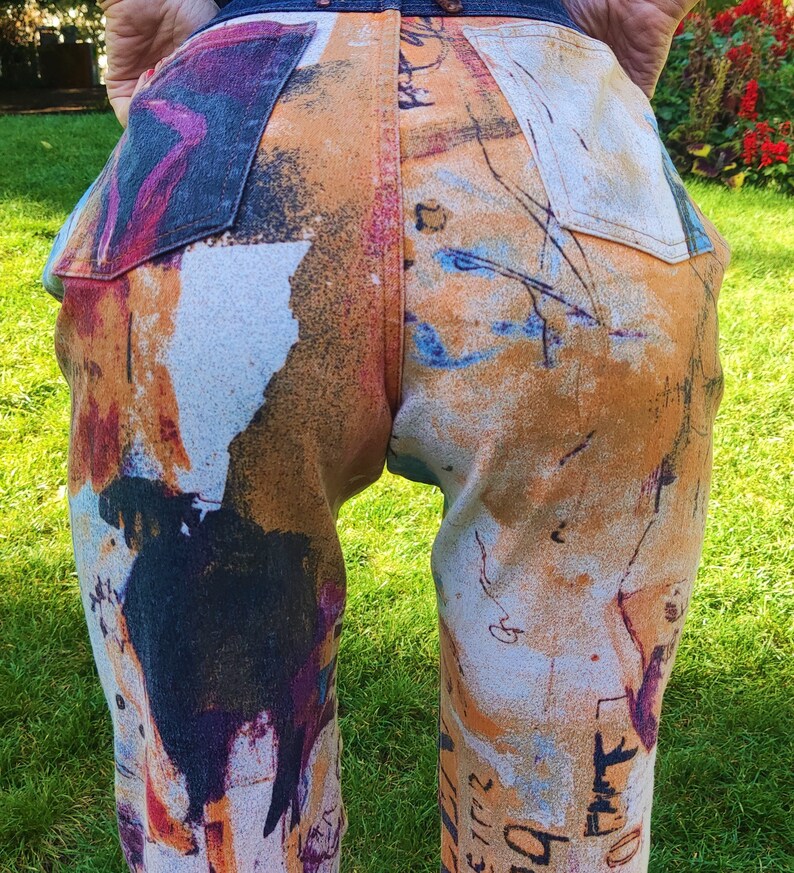 May include: A pair of jeans with a colorful abstract print. The print features a mix of orange, blue, white, and black colors. The jeans have a relaxed fit and a straight leg.
