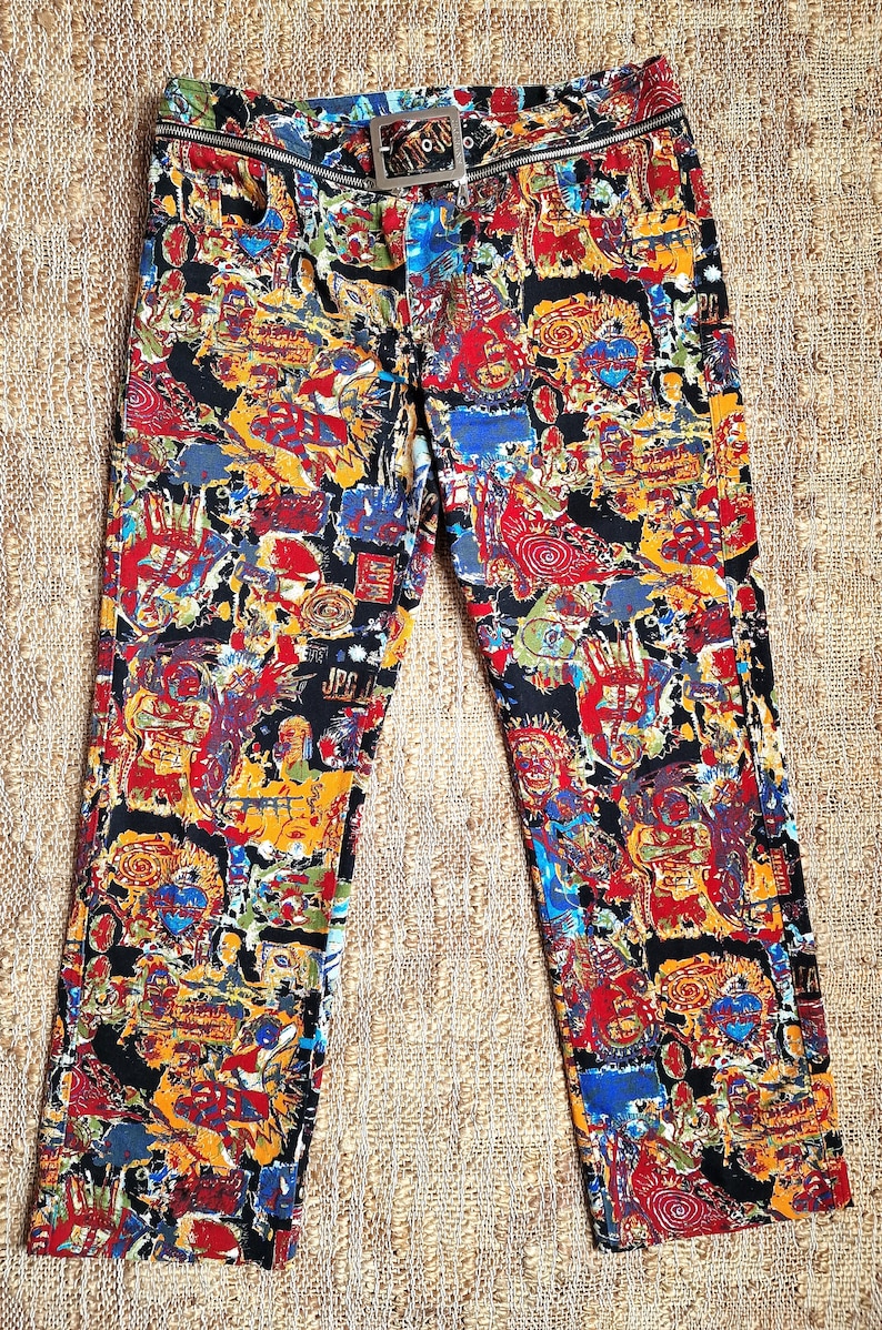May include: Black pants with a colorful abstract print. The pants have a silver zipper and a silver belt buckle.