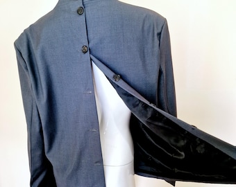 May include: A grey blazer with a high collar and a unique button closure down the back. The blazer is unbuttoned and the lining is visible.