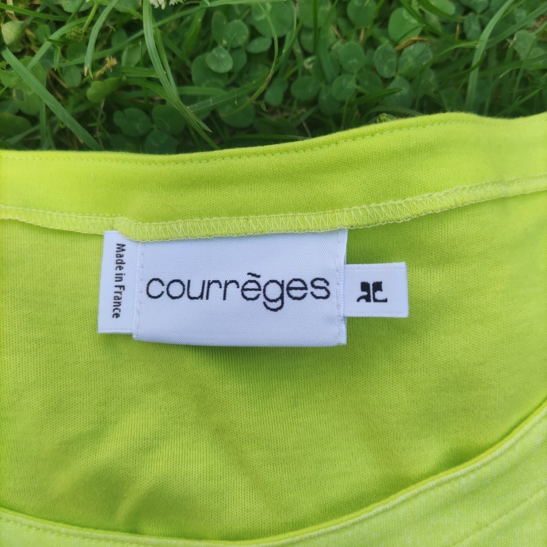 May include: A white tag with black text that reads "courr&egrave;ges" and "Made in France". The tag is attached to a lime green shirt.