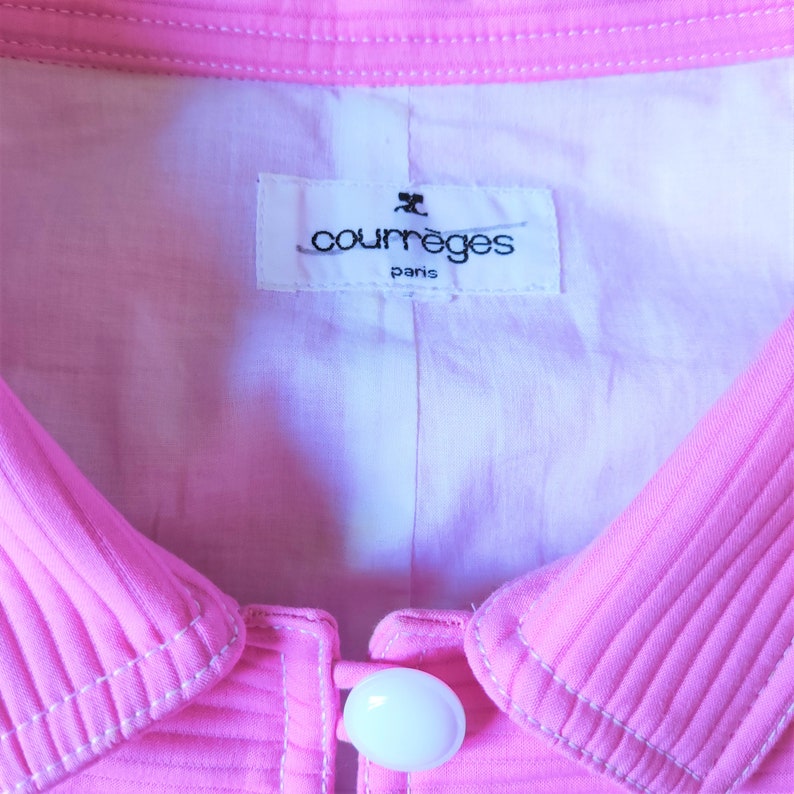 May include: A pink collared jacket with a white button and a white label that reads "Courr&egrave;ges Paris".