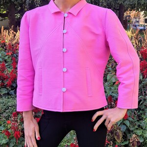 May include: A pink, ribbed, collared jacket with white buttons. The jacket has a slightly cropped length and a fitted silhouette.
