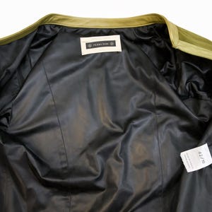 以下が含まれることがあります： オリーブグリーンのジャケット、黒いサテンの裏地付き。 ジャケットの内側が見え、裏地と衣服の構造がわかります。 サイズ42/10のタグが付いています。