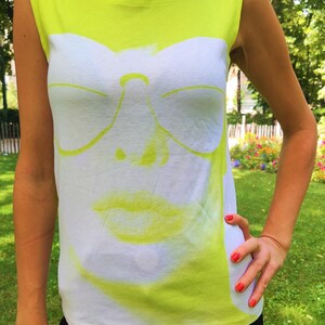 May include: A neon yellow sleeveless shirt with a white graphic print of a face wearing sunglasses and lipstick.