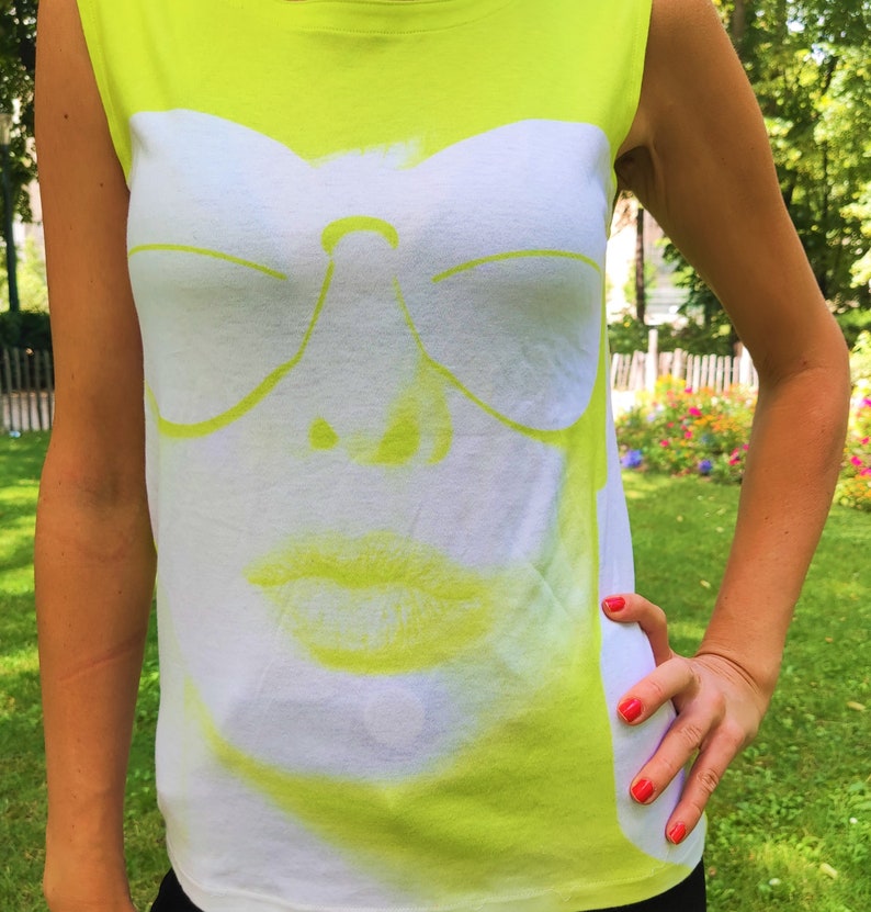 May include: A neon yellow sleeveless shirt with a white graphic print of a face wearing sunglasses and lipstick.