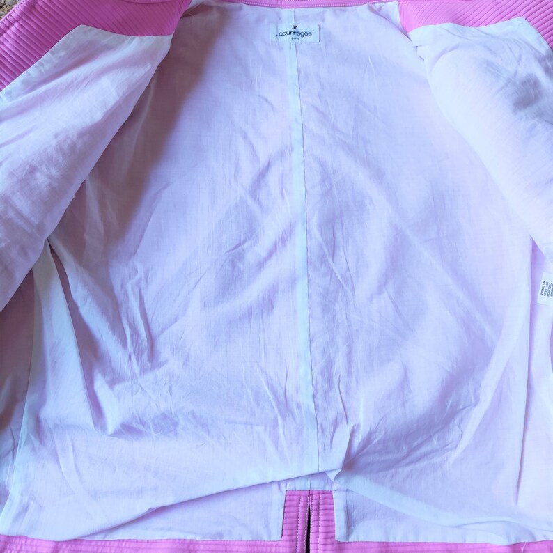 May include: The inside of a pink jacket with a white lining. The label reads "Courreges Paris".