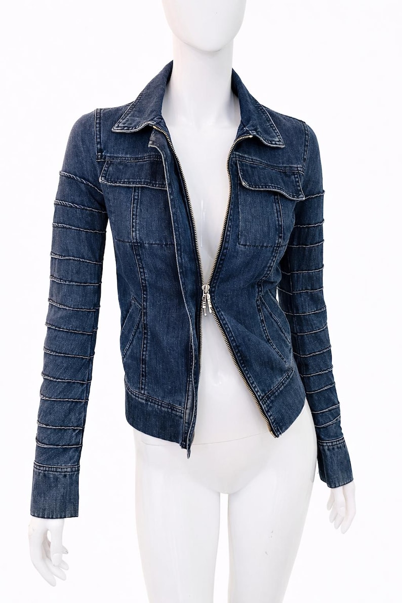 May include: A dark blue denim jacket with a zip-up front, two chest pockets, and decorative stitching on the sleeves. The jacket is displayed on a white mannequin.