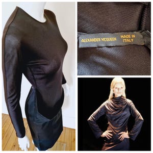 Puede incluir: Vestido negro de manga larga con cuello redondo y silueta entallada. El vestido presenta un panel en contraste en la falda. La etiqueta dice "ALEXANDER MCQUEEN MADE IN ITALY". El vestido se muestra en un maniquí.