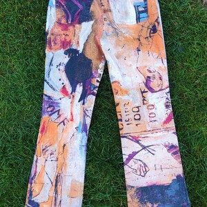 May include: A pair of blue denim jeans with a colorful abstract print. The print features a variety of colors, including orange, yellow, blue, and purple. The jeans have a bootcut style and are made of a soft, comfortable fabric.