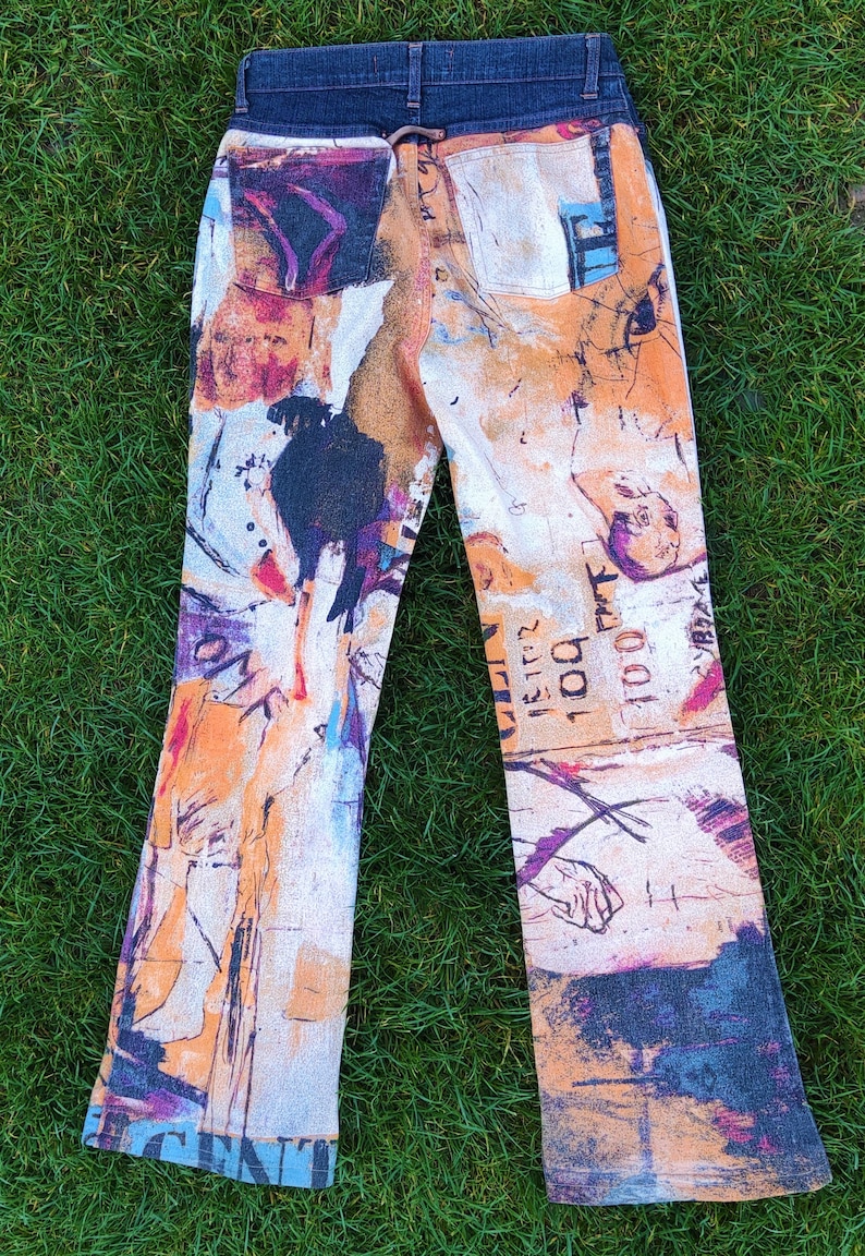 May include: A pair of blue denim jeans with a colorful abstract print. The print features a variety of colors, including orange, yellow, blue, and purple. The jeans have a bootcut style and are made of a soft, comfortable fabric.