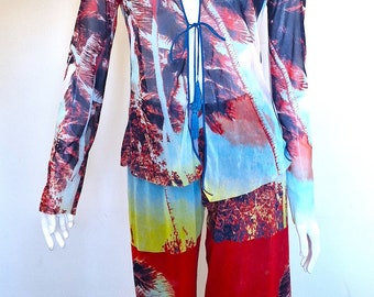 May include: A sheer, long-sleeved jumpsuit with a tropical print featuring palm trees and a tie at the neckline. The jumpsuit is red, blue, and yellow with a white background.