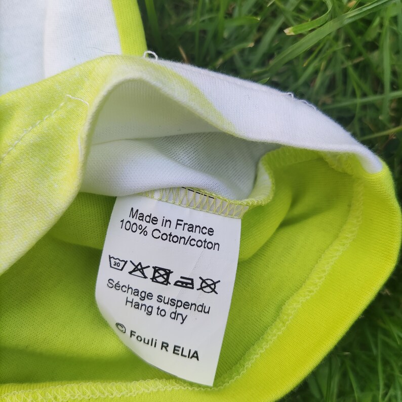 May include: White tag with black text that reads "Made in France 100% Coton/coton" and a black and white washing instruction symbol. Below the text is more black text that reads "S&eacute;chage suspendu Hang to dry" and a circle with the text "Fouli R ELIA".