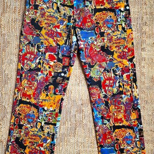 May include: Black pants with a colorful abstract print featuring a variety of shapes, lines, and figures. The pants have a zipper and a belt with a silver buckle.