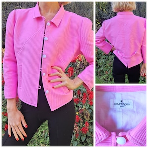 May include: A pink, ribbed, cropped jacket with a white button closure and a white label that reads "Courreges Paris".