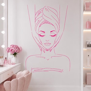 May include: A hot pink wall decal featuring a line art illustration of a person with eyes closed, wearing a towel wrap on their head, while hands perform a facial massage. The design depicts the head, shoulders, and upper chest area.