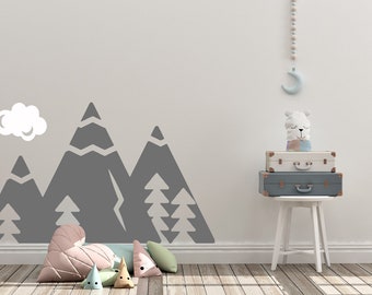 May include: A gray mountain range wall decal with white trees and a white cloud. A white stool with a stack of suitcases and a white stuffed animal on top. The room has a light wood floor.