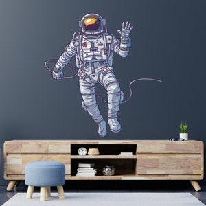 May include: A white astronaut with a blue and orange spacesuit is floating in space with a tether attached to their wrist. The astronaut is waving with their right hand. The background is a dark blue.