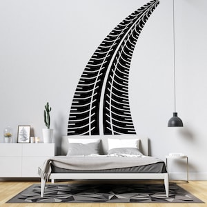 May include: Black tire track decal for a wall, shown above a bed with white bedding and a gray headboard. The decal is shaped like a curved tire track.