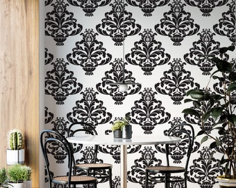 May include: A black and white damask patterned wallpaper with a dining table and four black chairs in front of it. The table is round and white with a gold base. There are two potted plants on the table and a hanging light fixture above the table.