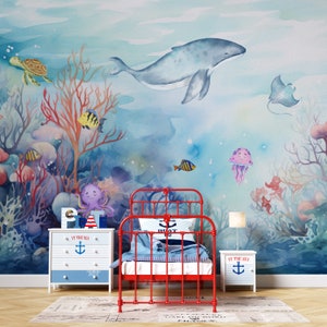 May include: A watercolor mural depicting an underwater scene with a whale, coral, fish, a turtle, a stingray, and a jellyfish. The mural is in a child's bedroom with a red metal bed frame and two white nightstands with the text "At the Sea" and an anchor.