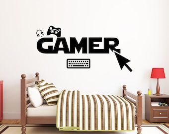 May include: Black and white wall decal with the word "GAMER" in large letters. The decal also includes a video game controller, headphones, a computer keyboard, and a mouse cursor.