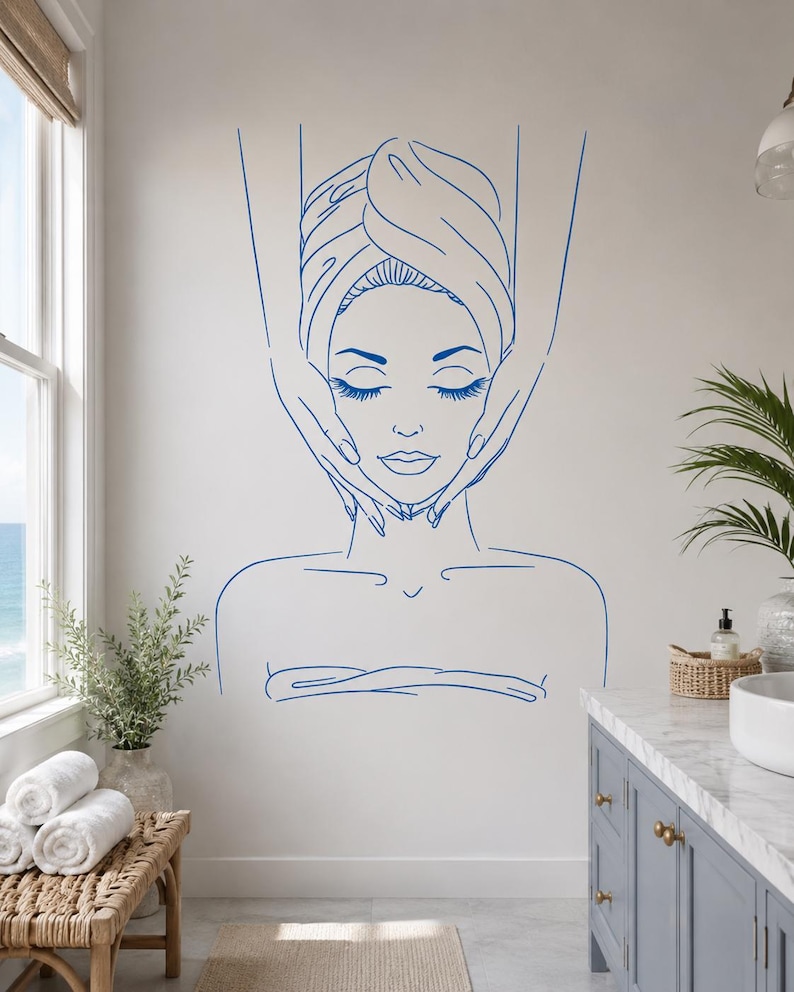 May include: A blue line art wall decal featuring a person with eyes closed, wrapped in a towel, receiving a facial massage. The design shows the person's head and shoulders with hands positioned on the sides of the face, rendered in simple strokes.